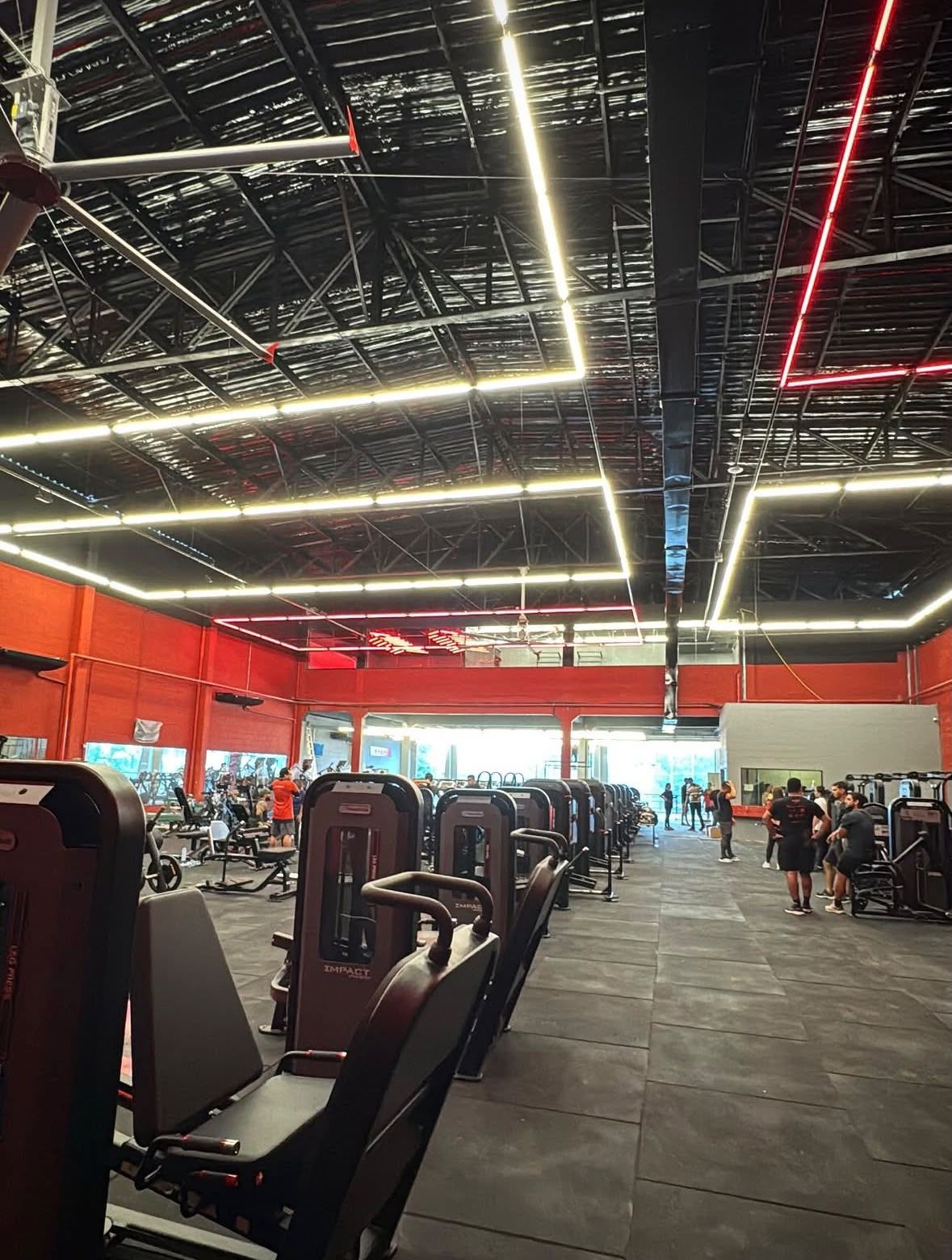Salão de musculação da Selfit Cohatrac em funcionamento, com aparelhos alinhados, alunos treinando e iluminação em linhas de LED sob a cobertura metálica.
